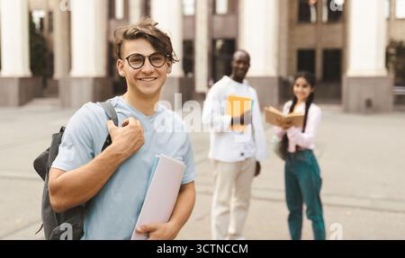 Student Kerl im Freien auf dem Campus mit seinen Klassenkameraden und Universitätsgebäude auf dem Hintergrund Stockfoto