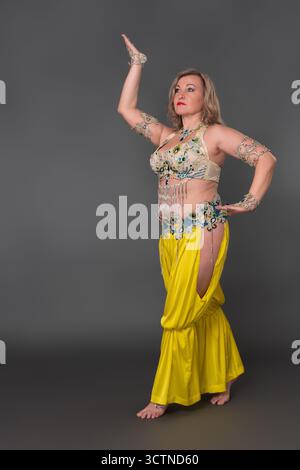 Vertrauensfrau Tänzerin mit ihrer Hand hochgezogenen Kleidung in Tanzkostüm - Oberteil und gelbe Haremshosen und sie trägt keine Schuhe, Performi Stockfoto