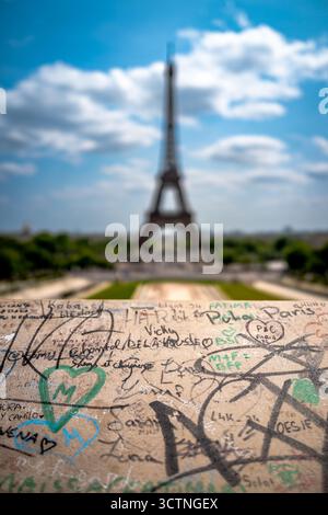Graffiti im Vordergrund mit verschwommenem Eiffelturm im Hintergrund unter hellem Himmel. Stockfoto