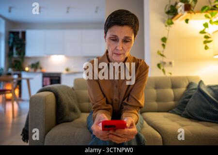 Traurige apathische reife Frau, die auf Nachrichten wartet, allein zu Hause Smartphone-Benachrichtigungen überprüft Stockfoto