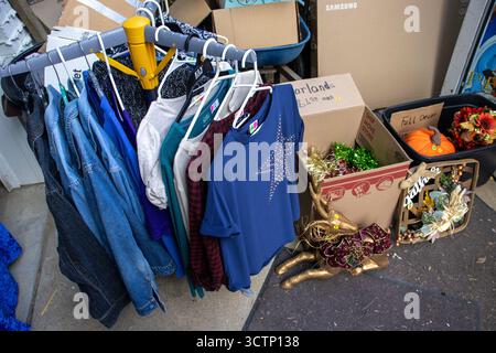 Hemden hängen auf einem Regal und Weihnachtsdekorationen zum Verkauf bei einem Garagenverkauf in einem Vorstadthaus im Mittleren Westen der USA. Stockfoto
