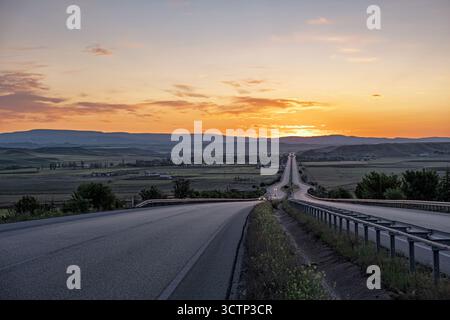 Malerischer Highway bei Sonnenuntergang. Ein atemberaubender Blick auf eine kurvenreiche Autobahn, die sich bis in die Ferne erstreckt. Dieses Bild fängt das Wesen von Reisen und Abenteuer ein Stockfoto