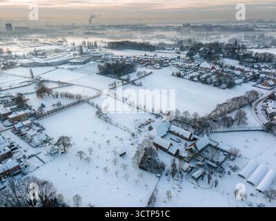 Luftaufnahme eines schneebedeckten Bauernhofs mit weißen Feldern, die sich nach außen erstrecken, mit der Stadt Brüssel im Hintergrund Stockfoto