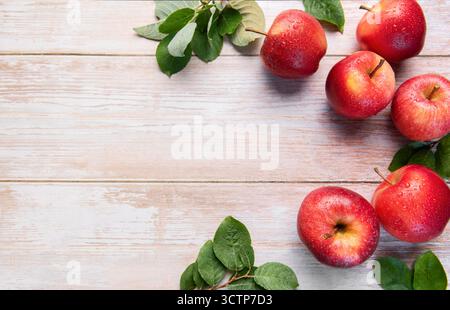 Frische rote Gala-Äpfel mit grünen Blättern und Wassertropfen auf rustikaler Holzoberfläche Stockfoto