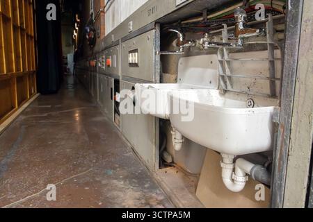 Die Doppelspülung befindet sich in einem Flur in einer Industriehalle mit freiliegenden Rohren und Chromarmaturen Stockfoto