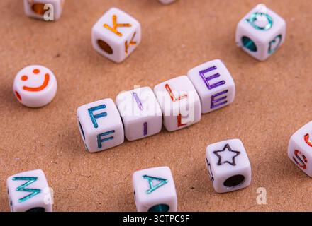 Weiße Buchstabenperlen mit der Schreibweise „DATEI“ sind auf einer braunen strukturierten Oberfläche angeordnet. Umgeben von anderen verstreuten Perlen, darunter ein Smiley-Gesicht und verschiedene l Stockfoto
