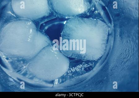 Nahaufnahme von Eiswürfeln in einem Glas kaltem Wasser. Makroaufnahme von Eiswürfeln, die in einem Glas mit kaltem Wasser schweben. Mit erfrischenden Texturen und Conden Stockfoto