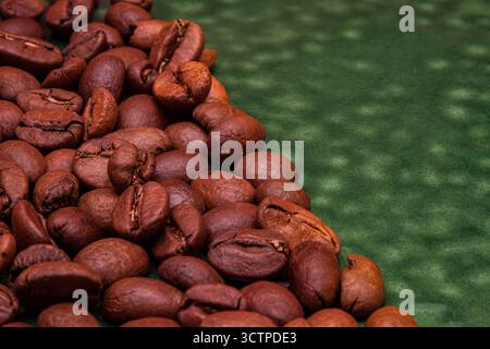 Makroansicht frisch gerösteter Kaffeebohnen auf strukturierter grüner Oberfläche. Mit satten Brauntönen und detaillierter Oberflächenstruktur. Stockfoto