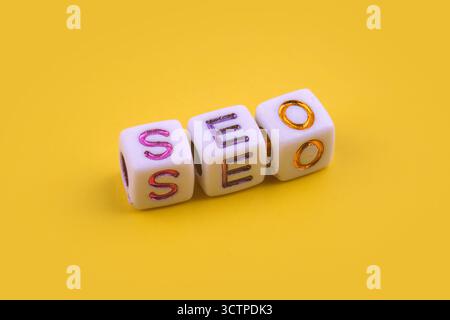 SEO-Akronym mit Buchstabenperlen. Buchstaben geben das Akronym „SEO“ (Search Engine Optimization) auf gelbem Hintergrund aus. Stockfoto