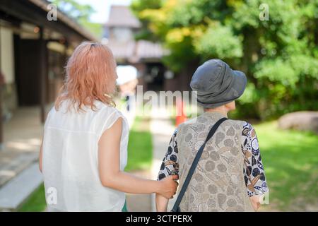 Zwei Frauen gehen zusammen, eine trägt ein rosafarbenes Hemd. Die Frau im rosa Hemd hält der anderen Frau den Arm Stockfoto