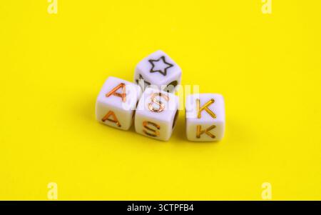 Vier kleine Kubikperlen auf hellgelbem Hintergrund. Drei Buchstaben zeigen goldene Buchstaben mit der Schreibweise „ASK“, während der vierte einen schwarz umrandeten Stern zeigt. Stockfoto