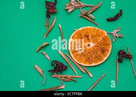 Flache Schicht getrockneter Orangenscheiben mit verschiedenen Kräutern und Blütenblättern auf grünem Hintergrund. Die Mischung aus Zitrusfrüchten und pflanzlichen Zutaten lässt natürliche Teezutaten vermuten Stockfoto