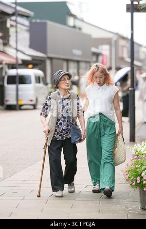 Zwei Frauen gehen die Straße entlang, eine hält einen Stock. Die Frau mit dem Stock ist älter und die andere jünger Stockfoto