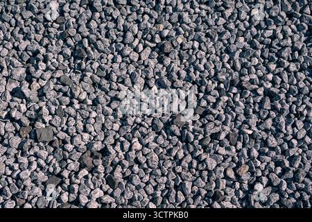 Nahaufnahme kleiner Kiessteine, die einen einheitlichen strukturierten Hintergrund bilden. Natürliche graue Steine unter Sonnenlicht schaffen eine robuste und realistische Oberfläche. Stockfoto
