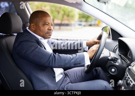 Ein ernster schwarzer Geschäftsmann sitzt im Auto, hupend, während er das Lenkrad hält Stockfoto