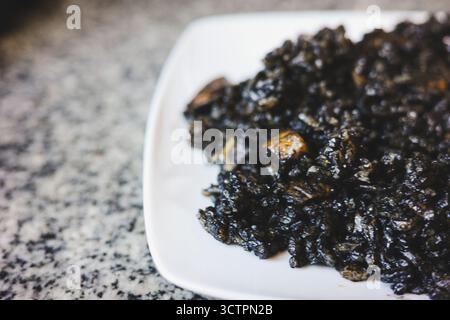 Schwarzer spanischer Reis mit Tintenfischtinte, serviert auf einem weißen Teller, traditionelles mediterranes Gericht mit Meeresfrüchten Stockfoto