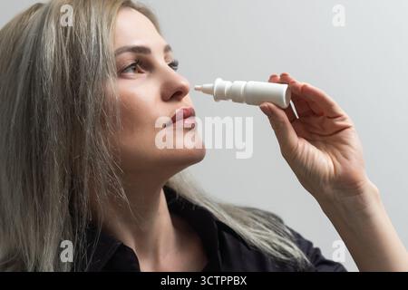 Eine Frau mit laufender Nase hält ein Medikament in der Hand. Stockfoto