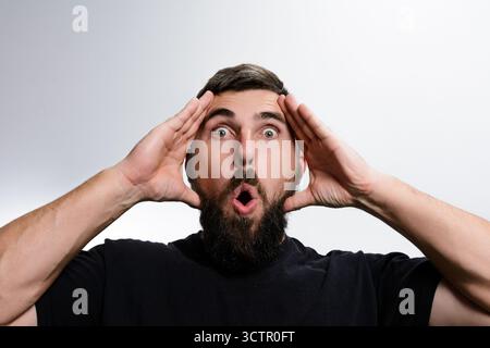 Überraschter Mann mit Bart und offenem Mund vor weißem Hintergrund Stockfoto
