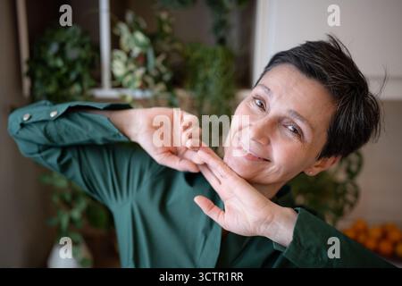 Lächelnde ältere Frau tanzt zu Hause verspielt, schau in die Kamera in fröhlichem Ausdruck. Natürliche Schönheit Stockfoto