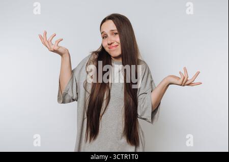 Eine junge Frau mit langen Haaren, die mit den Schultern zuckt und Verwirrung ausdrückt. Stockfoto
