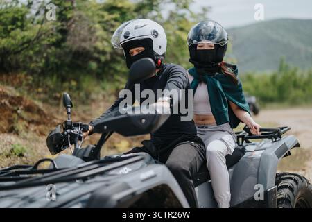 Zwei Freunde, die mit einem ATV durch das Gelände im Freien fahren und dabei Schutzausrüstung tragen Stockfoto