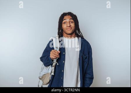 Junger Mann mit Dreadlocks, der einen Rucksack hält und legere Kleidung trägt. Stockfoto