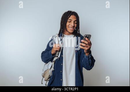 Junger Mann mit Rucksack, der auf das Smartphone blickt, lächelt. Stockfoto