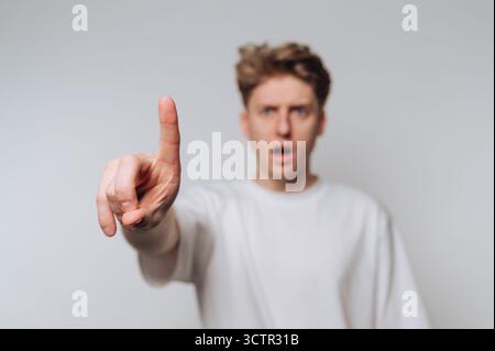 Junger Mann in weißem Hemd, der mit überraschtem Ausdruck zeigt. Stockfoto