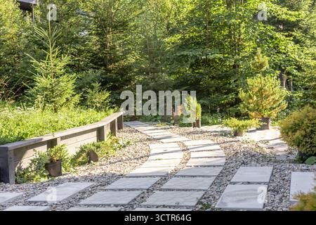 Ein ruhiger Gartenweg aus Steinplatten schlängelt sich durch üppiges Grün. Kleine Pflanzen und Bäume säumen den Weg und schaffen einen ruhigen Außenbereich. Stockfoto