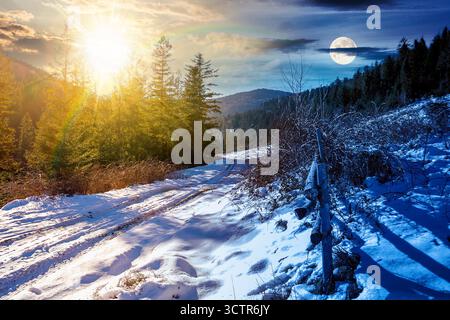 Wintersonnenwende in bergiger Landschaft. Tag- und Nachtzeitwechsel. Holzzaun entlang der Straße durch Nadelwald in der Nähe von Schnee bedeckt Stockfoto