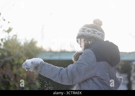 Achtsames Kind steht an schneebedeckten Tagen draußen und beobachtet Schnee in der Hand, Symbol für Bewusstsein, Neugier und ruhige Verbindung mit der Natur Stockfoto