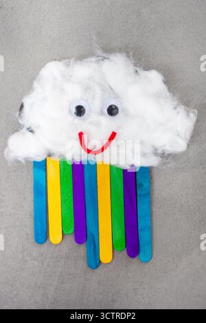 Eine Wolke aus Baumwollwolle mit guten Augen und einem Lächeln. Unter der Wolke befindet sich ein Regenbogen aus Eisstöcken Stockfoto