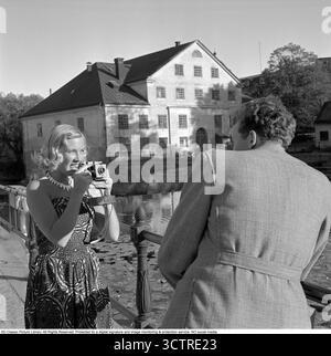 Die junge blonde Frau wird mit einer Kamera gesehen und zeigt auf den Mann, um ein Foto zu machen. 1951. Conard Ref. 1752 Stockfoto