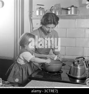 1956 stehen Mutter und Tochter am Gasherd und bereiten gemeinsam ein Abendessen vor. Hinter ihnen befindet sich die klassische „Visseljohanna“, die pfeifende Kaffeekanne. (Conard Ref. 3159) Stockfoto
