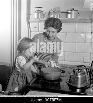 1956 stehen Mutter und Tochter am Gasherd und bereiten gemeinsam ein Abendessen vor. Hinter ihnen befindet sich die klassische „Visseljohanna“, die pfeifende Kaffeekanne. (Conard Ref. 3159) Stockfoto