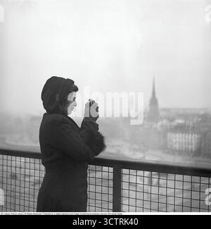 Spionin, 1941. Dieses Bild zeigt eine Spionin, die List und Täuschung nutzt, um Informationen von Militärpersonal zu sammeln. Während des Zweiten Weltkriegs wurde die schwedische Öffentlichkeit angewiesen, keine Informationen zu teilen, egal wie trivial sie auch sein mögen – dies wurde als „der Spion baut das Puzzle zusammen“ bezeichnet. In dieser Szene fotografiert die Spionin mit einer Kamera das Hafengebiet von Stadsgården in Stockholm. Schweden, 1941. Kristoffersson Ref. 225-36. Stockfoto