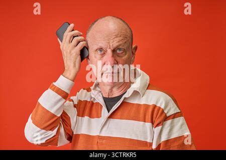 Nahaufnahme Porträt eines älteren Mannes im Studio am Telefon auf oranje Hintergrund Stockfoto