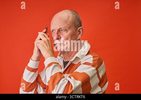 Nahaufnahme Porträt eines älteren Mannes im Studio am Telefon auf oranje Hintergrund Stockfoto
