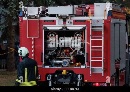 Rückansicht eines roten Feuerwehrwagens mit geöffnetem Fach, der die komplexe Pumpenverkleidung, die Anzeigen und die Ausrüstung freigibt, während ein Feuerwehrmann in der Nähe steht. Stockfoto