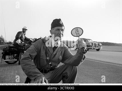 Polizei-Verkehrsüberwachung auf Riksettan, 1958. Zwischen 1945 und 1962 diente die Riksväg 1 als Hauptautobahn zwischen Helsingborg und Stockholm. Heute ist diese Strecke Teil der europäischen Route E4. Ein auf einem BMW Motorrad montierter Motorradpolizist und ein Polizist mit einem Schild Polizei steht am Straßenrand, überwacht den Verkehr und ist bereit, das nächste Auto zur Kontrolle zu bringen. Schweden, 1958. In den 1950er Jahren, als der Automobilverkehr im wachsenden schwedischen Straßennetz zunahm, spielten Polizeipatrouillen eine entscheidende Rolle bei der Gewährleistung der Straßenverkehrssicherheit und der Strafverfolgung. Motorzyklusmotor Stockfoto