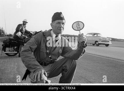 Polizei-Verkehrsüberwachung auf Riksettan, 1958. Zwischen 1945 und 1962 diente die Riksväg 1 als Hauptautobahn zwischen Helsingborg und Stockholm. Heute ist diese Strecke Teil der europäischen Route E4. Ein auf einem BMW Motorrad montierter Motorradpolizist und ein Polizist mit einem Schild Polizei steht am Straßenrand, überwacht den Verkehr und ist bereit, das nächste Auto zur Kontrolle zu bringen. Schweden, 1958. In den 1950er Jahren, als der Automobilverkehr im wachsenden schwedischen Straßennetz zunahm, spielten Polizeipatrouillen eine entscheidende Rolle bei der Gewährleistung der Straßenverkehrssicherheit und der Strafverfolgung. Motorzyklusmotor Stockfoto