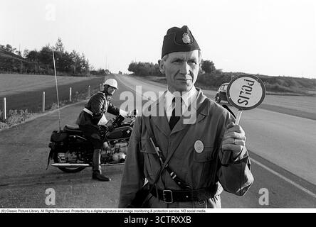 Polizei-Verkehrsüberwachung auf Riksettan, 1958. Zwischen 1945 und 1962 diente die Riksväg 1 als Hauptautobahn zwischen Helsingborg und Stockholm. Heute ist diese Strecke Teil der europäischen Route E4. Ein auf einem BMW Motorrad montierter Motorradpolizist und ein Polizist mit einem Schild Polizei steht am Straßenrand, überwacht den Verkehr und ist bereit, das nächste Auto zur Kontrolle zu bringen. Schweden, 1958. In den 1950er Jahren, als der Automobilverkehr im wachsenden schwedischen Straßennetz zunahm, spielten Polizeipatrouillen eine entscheidende Rolle bei der Gewährleistung der Straßenverkehrssicherheit und der Strafverfolgung. Motorzyklusmotor Stockfoto