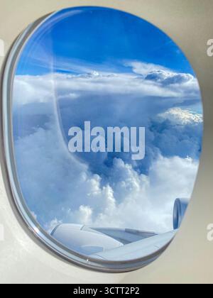 Blick eines Fluggastes durch das Bullauge oder Fenster über dem blauen Himmel mit verstreuten Wolken über dem Indischen Ozean in Richtung Western Australi Stockfoto