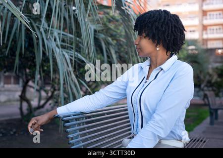 Eine schwarze Frau, die im Profil und tief in Gedanken gesehen wurde, sitzt auf einer Bank im Park. Stockfoto