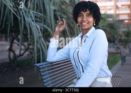 Eine selbstbewusste schwarze Frau posiert in die Kamera, während sie auf einer Parkbank sitzt. Stockfoto