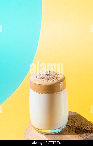 Trendiges Koreanisches Getränk. Dalgona Kaffee mit üppigem Schaum in einem Glas auf einem gelben und türkisfarbenen Hintergrund. Stockfoto