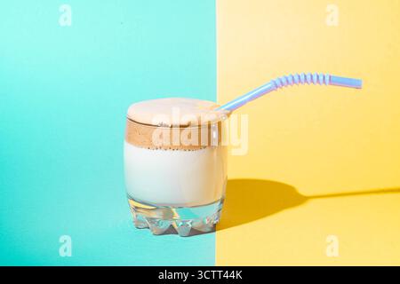 Dalgona-Kaffee mit üppigem Schaum in einem Glas auf gelbem und blauem Hintergrund. Trendiges Koreanisches Getränk. Stockfoto