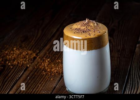 Dalgona-Kaffee mit üppigem Schaum in einem Glas auf hölzernem Hintergrund. Low-Key-Foto. Weichzeichner Stockfoto