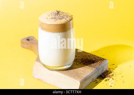 Dalgona-Kaffee mit üppigem Schaum in einem Glas auf einer Holzleiste auf gelbem Hintergrund. Trendiges Koreanisches Getränk. Stockfoto