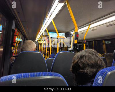 In einem modernen Stadtbus: Blaue Sitze, gelbe Pole und Passagiere auf einer täglichen Fahrt Stockfoto